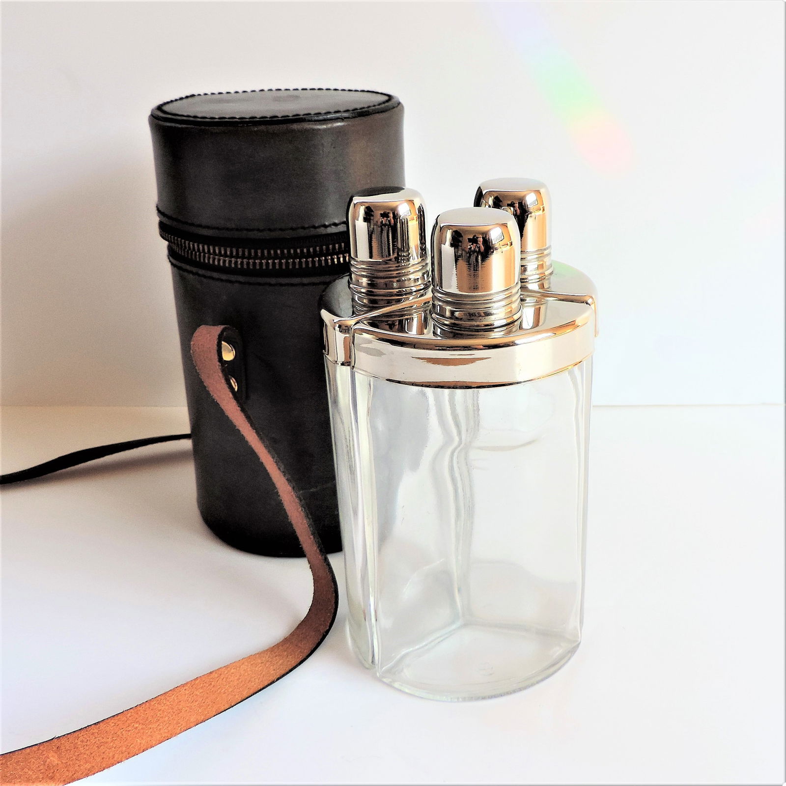 ART DECO TRIPLE GLASS FLASK SET IN LEATHER CASE. Circa 1930's flask set featuring three wedge-shaped: ART DECO TRIPLE GLASS FLASK SET IN LEATHER CASE. Circa 1930's flask set featuring three wedge-shaped flasks with silver plated cap, neck & shoulders fitted nicely in a cylindrical leather carrying cas