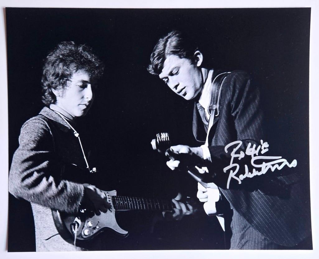 Robbie Robertson In-Person Signed 10” x 8” Photo w/ Dylan (Third Party Guaranteed): Black and white 10" x 8" photo signed in silver felt tip marker by The Band's Robbie Robertson. The image features Robertson on stage performing alongside Bob Dylan. In fine condition. Obtained in-per