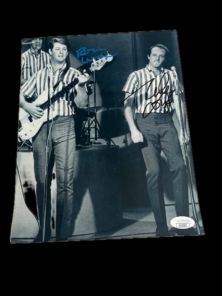 The Beach Boys: Wilson & Love Dual-Signed Photo (2 Sigs) (JSA Authentication): Black and white 8” x 10” photo of the Beach Boys performing signed in blue paint pen by Brian Wilson and black felt tip marker by Mike Love. In fine condition. Accompanied by JSA 