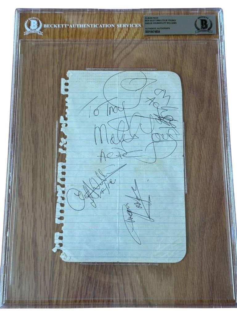 AC/DC Fully Group Signed Vintage w/ Bon Scott Notebook Page (4 Sigs) (Beckett/BAS Authentication): White lined 7.5" x 5" notebook page signed in black ballpoint pen by AC/DC band members Bon Scott, Malcolm Young (who inscribed “To Troy” and “AC/DC” before and after his signa