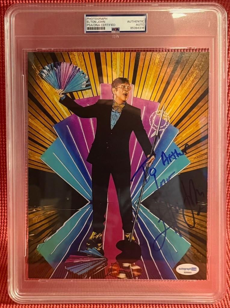 Elton John Signed Slabbed 10" x 8" Photo (PSA DNA Authentication): Color 10" x 8" slabbed photo signed in blue felt tip marker by musician Elton John, who also added the inscription "To Arthur Love" before his signature. In fine condition. Encapsulated and