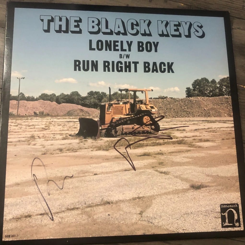The Black Keys Group Signed "Lonely Boy" Album (2 Sigs) (JSA Authentication): "Lonely Boy" album signed on the cover in blue felt tip marker by The Black Keys band members Dan Auerbach and Patrick Carney. Measuring approximately 12" x 12" and in fine condition. Obtained in-pers
