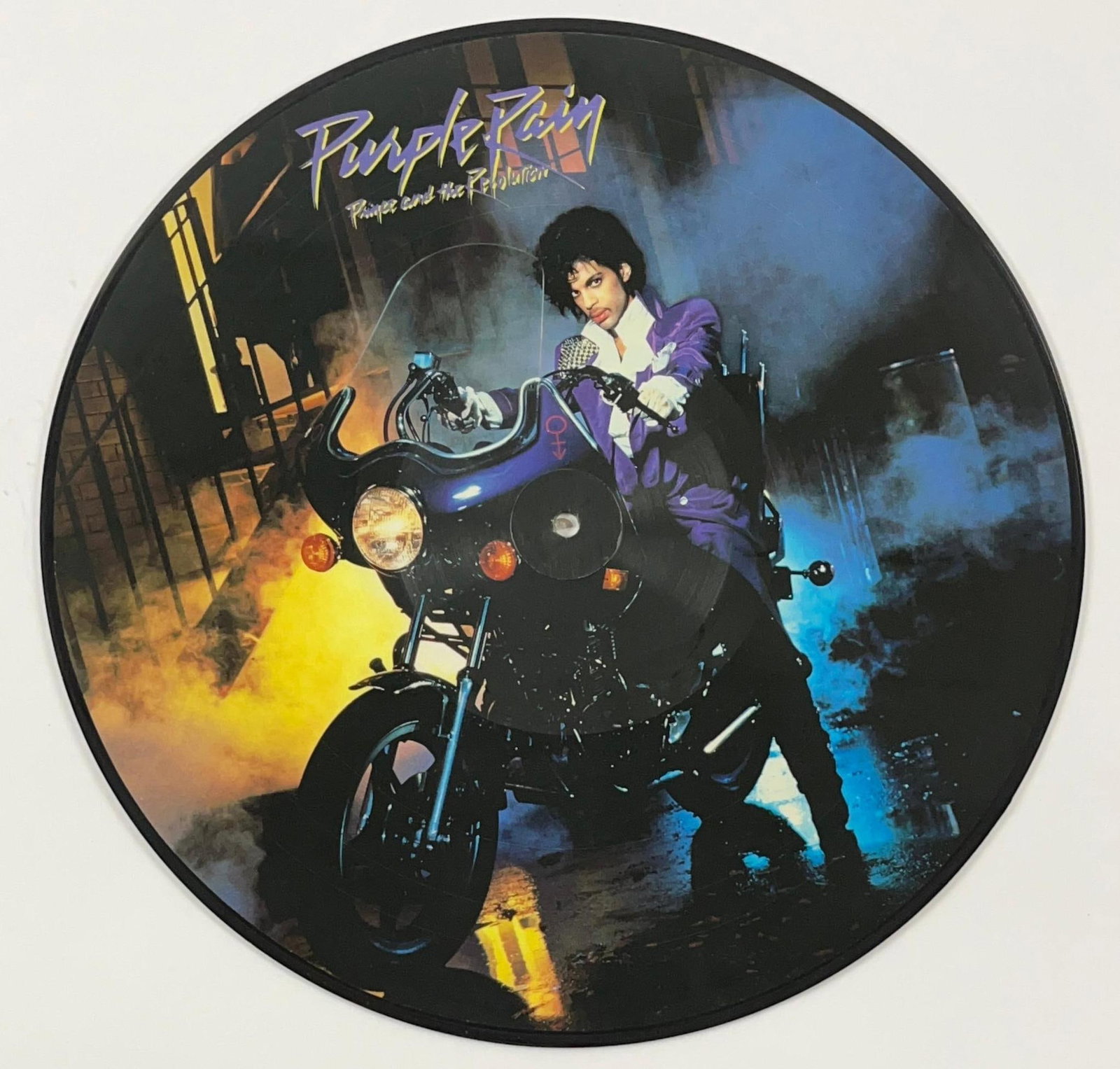 Prince "Purple Rain" Picture Disc W/ Original Plastic Sleeve: "Purple Rain" picture disc. Measuring approximately 12" x 12" and in fine condition. Disc comes in original Discoleccion brand clear plastic case, featuring the album's track listing in Spanish on