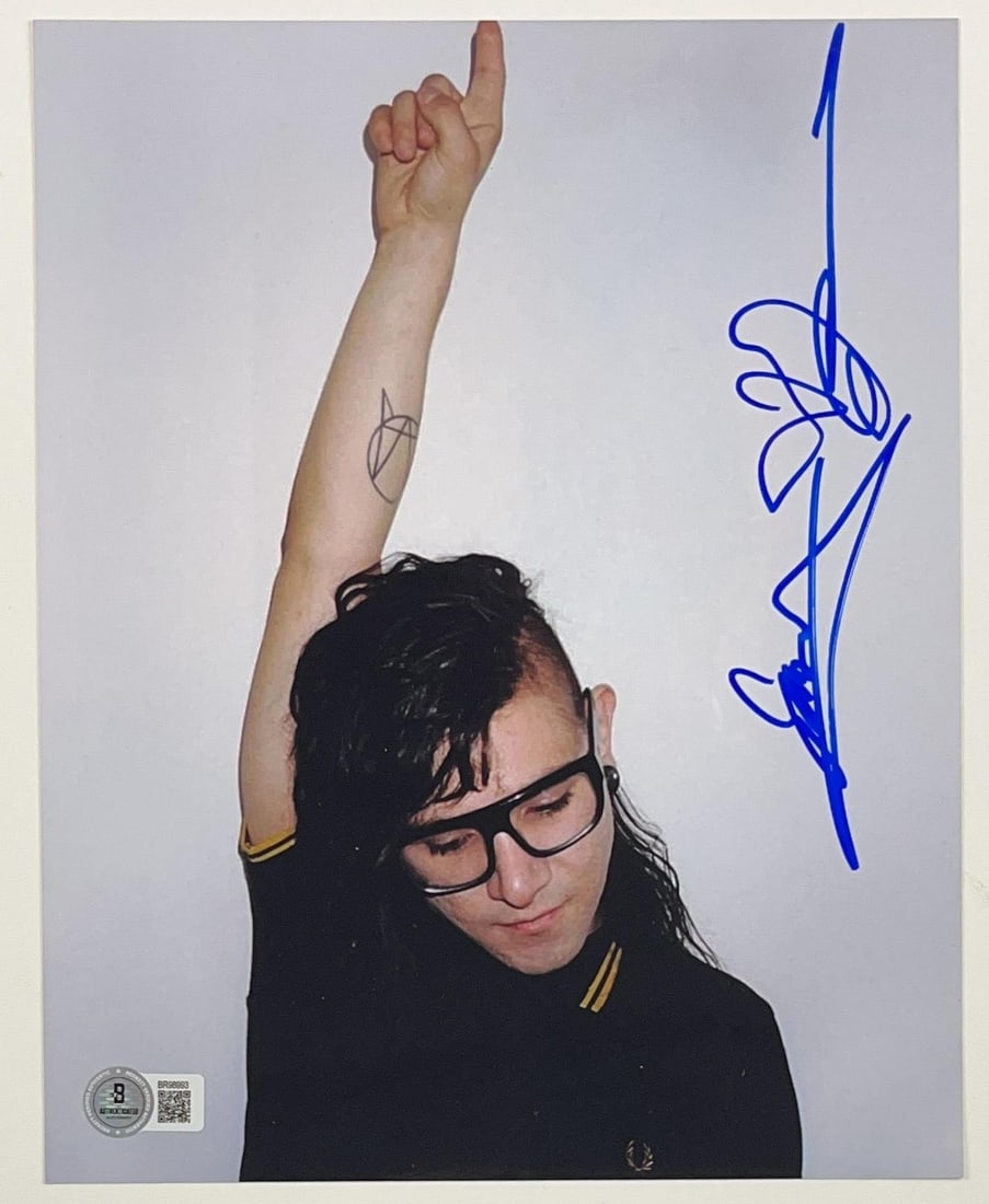 Skrillex Signed 10" x 8" Photo (Beckett Authentication): Color 10" x 8" photo signed in blue felt tip marker by musician Skrillex. In fine condition. Authenticated by Beckett, with their official hologram affixed to the front bottom left corner (#BR98993)-