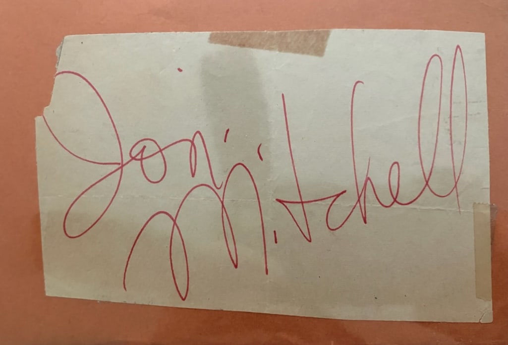 Joni Mitchell Signed 4.5" x 6.5" Cut (Beckett Authentication): Off-white 4.5" x 6.5" cut signed in red ballpoint pen by musician Joni Mitchell. In very good condition, with some signs of scattered wear, including a very small tear on the upper left corner, and a