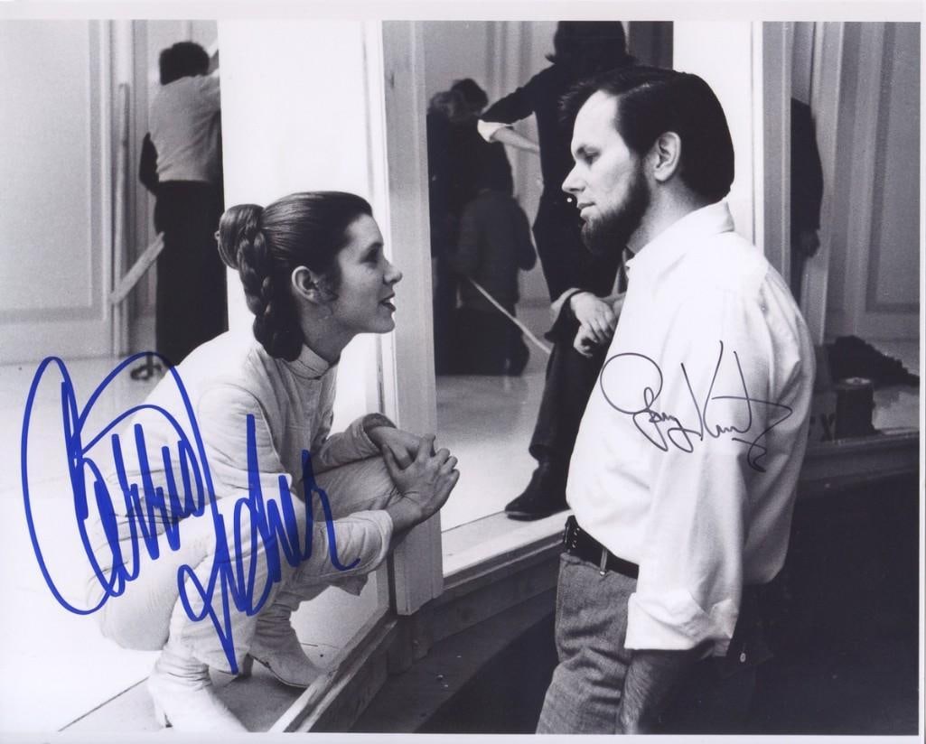 Star Wars: Carrie Fisher & Gary Kurtz Signed 8" x 10" Photo (2 Sigs) (Third Party Guaranteed): Black-and-white 8" x 10" photo of the behind-the-scenes making of the film "Star Wars: Empire Strikes Back," signed in blue and black felt tip markers by actress Carrie Fisher and producer Gary Kurtz.