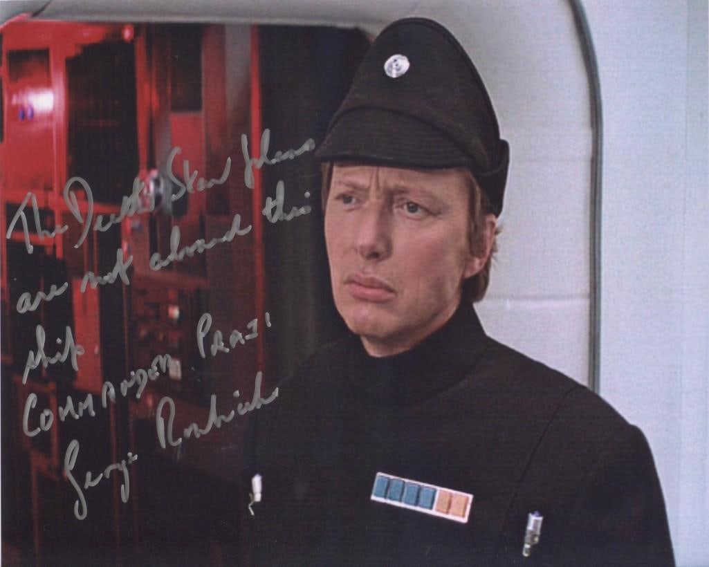 Star Wars: George Roubicek Signed 8" x 10" Photo (Third Party Guaranteed): Color 8" x 10" photo of the character Commander Praji from the film "Star Wars: A New Hope," signed in silver felt tip marker by actor George Roubicek. Roubicek also inscribed the message "The Death