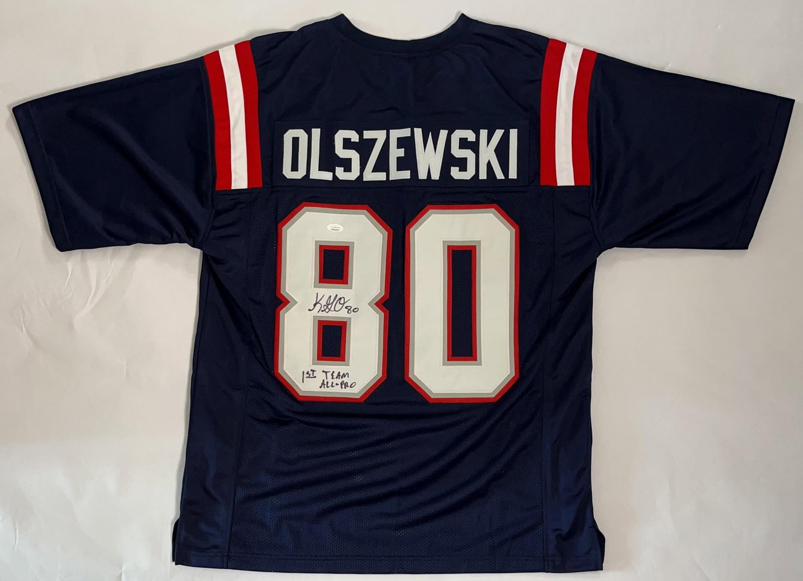 Gunner Olszewski Signed New England Patriots Jersey #80 (JSA Authentication): Blue 34" x 24" signed New England Patriots jersey #80 signed on the back numbering in black felt tip marker by former player Gunner Olszewski, who also inscribed his number "80" and "1st Team
