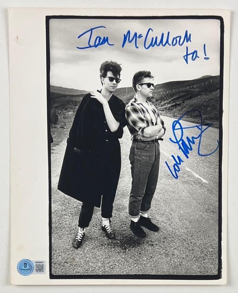 Echo & the Bunnymen: Ian McCulloch Signed 10" x 8" Press Photo (Beckett Authentication): Black-and-white 10" x 8" press heavy-weight paper photo signed in blue felt tip marker by Echo & the Bunnymen band member Ian McCulloch, who also inscribed "Ta!" and his printed name before his signat