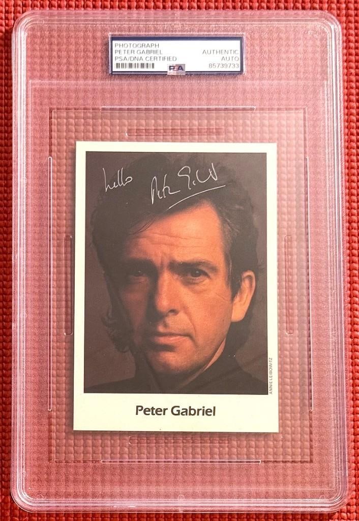 Genesis: Peter Gabriel Signed 6" x 4" Photo (PSA/DNA Encapsualted): Color 6" x 4" photo signed in silver felt tip marker by Genesis band member Peter Gabriel, who also inscribed "Hello" before his signature. In fine condition. Encapsulated and authenticated by