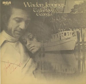 Waylon Jennings Signed "Cedartown Georgia" Album (ACOA Authentication): "Cedartown Georgia" album signed on the cover in red ballpoint pen by musician Waylon Jennings. Measuring approximately 12" x 12" and in fine condition. Record is included. Accompanied by a full