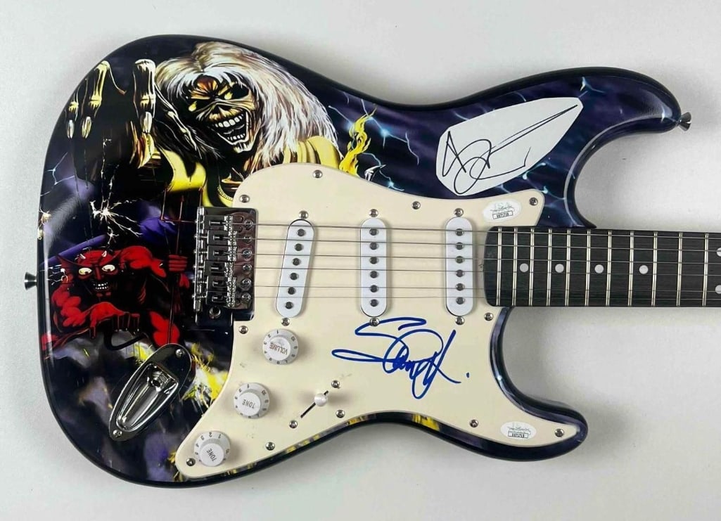 Iron Maiden Group Signed "Eddie" Custom Graphics Stratocaster-Style Electric Guitar (2 Sigs) (JSA): "Eddie" custom graphics Stratocaster-style electric guitar signed on the pickguard and sticker in black and blue felt tip markers by Iron Maiden band members Bruce Dickinson and Steve Harris. Measurin