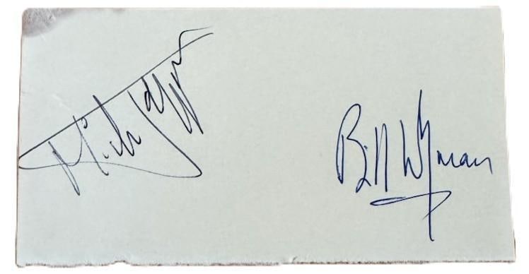 The Rolling Stones: Mick Jagger & Bill Wyman Signed Album Page (2 Sigs) (Grad): White paper 2.5" x 5" album page signed in black and blue ballpoint pens by the Rolling Stones band members Bill Wyman and Mick Jagger. In very good condition, with some signs of scattered wear,