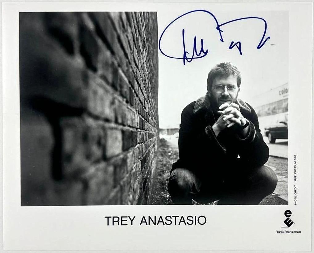 Phish: Trey Anastasio Signed Promotional Photo (Third Party Guaranteed): Black and white promotional photo of Phish guitarist and vocalist Trey Anastasio, signed in blue felt tip marker across the top. Photo depicts Anastasio crouched against a brick wall. Measuring approx