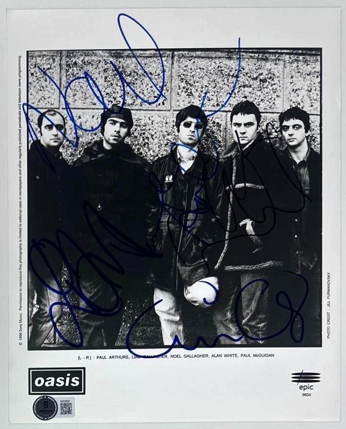 Oasis Fully Group Signed 8" x 10" Promo Photo (5 Sigs) (Beckett Authentication): Black-and-white 8" x 10" promotional photo signed in blue felt tip marker by Oasis band members Noel Gallagher, Liam Gallagher, Paul McGuigan, Paul Arthurs, and Alan White. In fine condition.