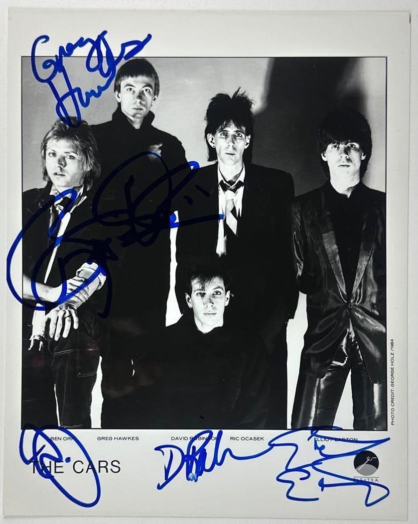 The Cars Fully Group Signed 10" x 8" Promo Photo (5 Sigs) (JSA Authentication): Black-and-white 10" x 8" promotional photo signed in blue felt tip marker by The Cars band members Greg Hawkes, Elliott Easton, Ric Ocasek, Benjamin Orr, and David Robinson. In fine condition.