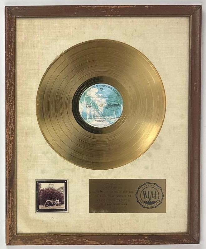 America "Holiday" RIAA Certified Sales Award Presented to Chip Rachlin: RIAA Certified Sales Award presented to Chip Rachlin to commemorate the sale of more than $1,000,000 worth of the Warner Bros. Records album "Holiday" by America. The vintage white matte framed displa