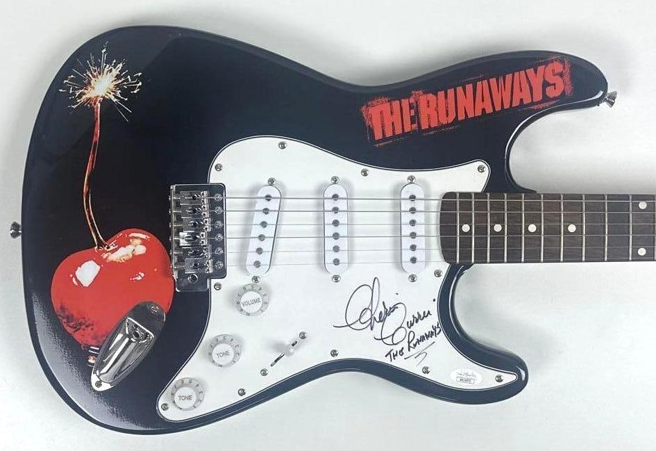 The Runaways: Cherie Currie Signed Cherry Bomb Graphics Stratocaster-Style Guitar (JSA): Cherry Bomb graphics Stratocaster-style guitar signed on the pickguard in black felt tip marker by the Runaways band member Cherie Currie, who also inscribed the band name "The Runaways" under her