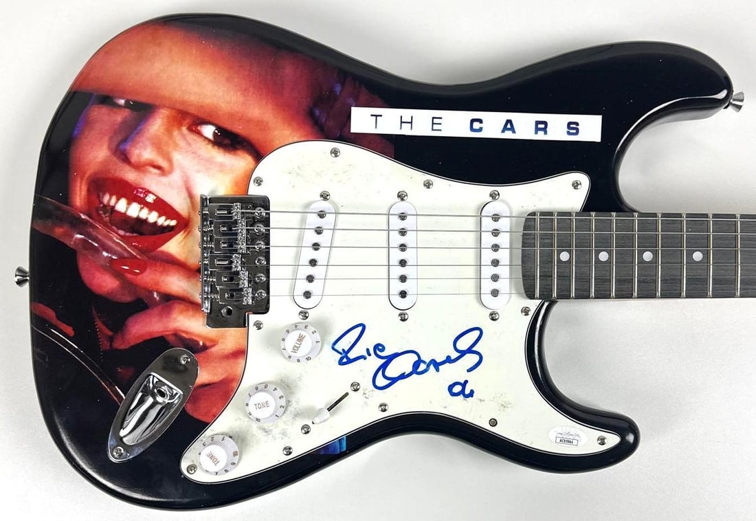 The Cars: Ric Ocasek Signed "The Cars" Album Graphics Stratocaster-Style Guitar (JSA): "The Cars" album custom graphics Stratocaster-style guitar signed on the pickguard in blue felt tip marker by The Cars band member Ric Ocasek. Measuring approximately 39" x 13" and in fine condition.