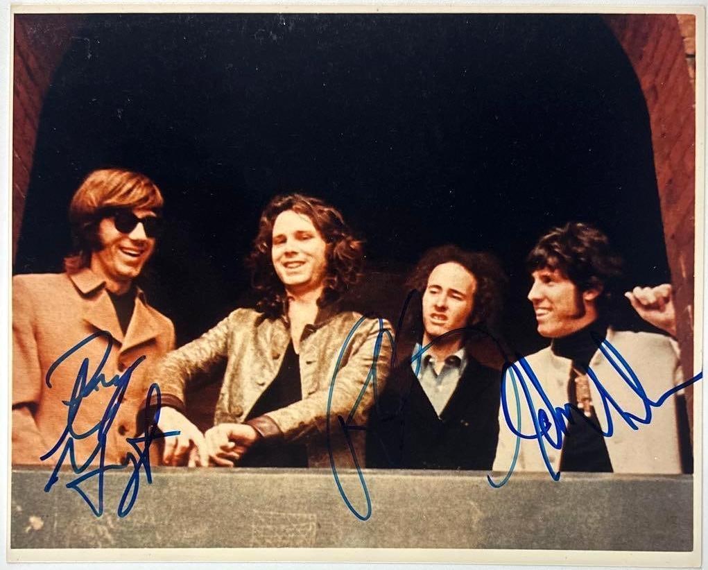 The Doors Group Signed 8" x 10" Photo (3 Sigs) (JSA Authentication): Color 8" x 10" photo signed in blue felt tip marker by The Doors band members Ray Manzarek, John Densmore, and Bobby Krieger. In fine condition. Authenticated by JSA. Provenance This piece was