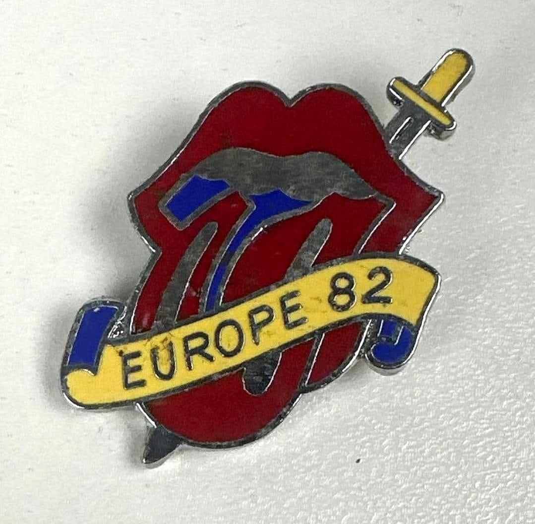 The Rolling Stones Vintage Original "Europe 82" Pin (Chip Rachlin Collection): Vintage original 1.5" x 1" red, blue, and yellow silver pin of the Rolling Stones tongue sticking-out logo in red and blue, with a yellow banner across the tongue reading "Europe 82" and the yellow