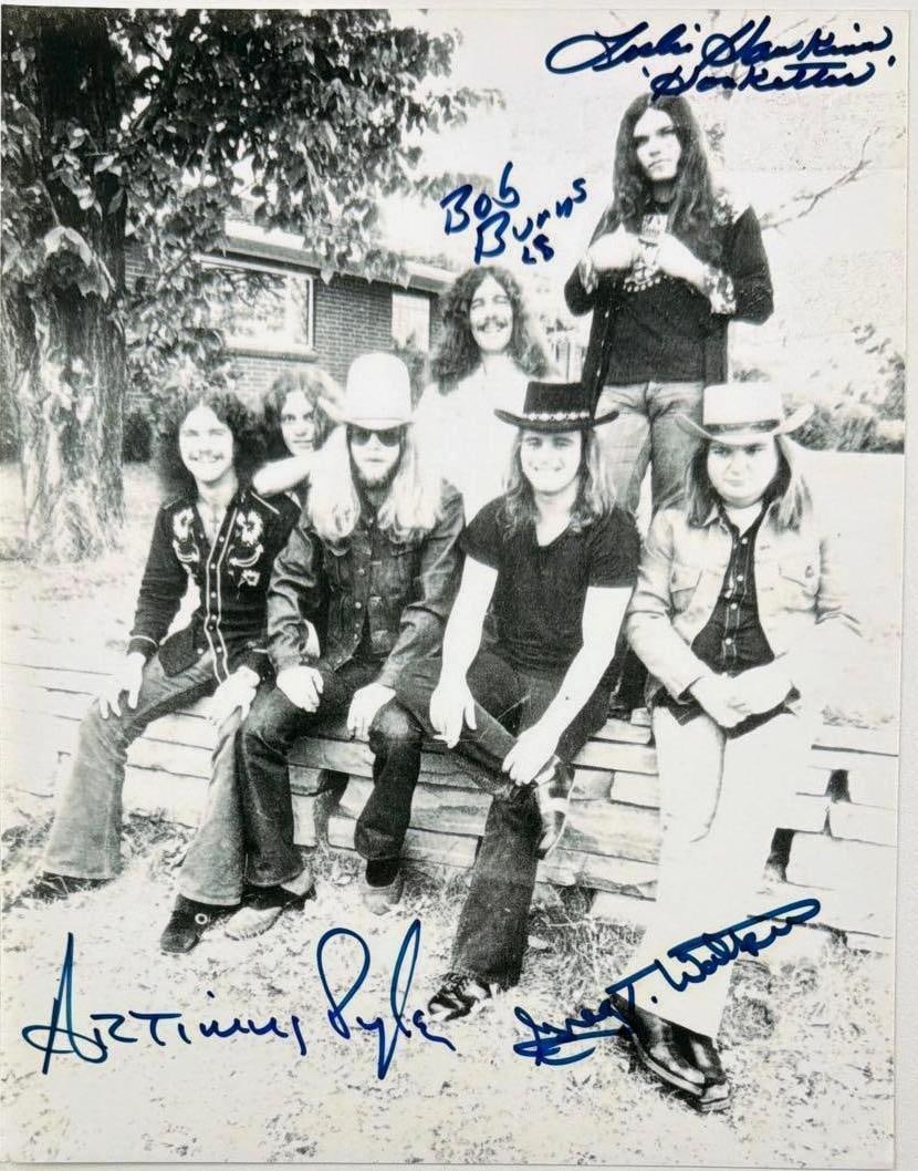 Lynyrd Skynyrd Group Signed 10" x 8" Laser Print Photo (4 Sigs) (Beckett): Black-and-white 10" x 8" laser print photo signed in blue felt tip marker by Lynyrd Skynyrd band members Artimus Pyle, Bob Burns, who inscribed "LS" after his signature, Leslie Hawkins, who inscribed