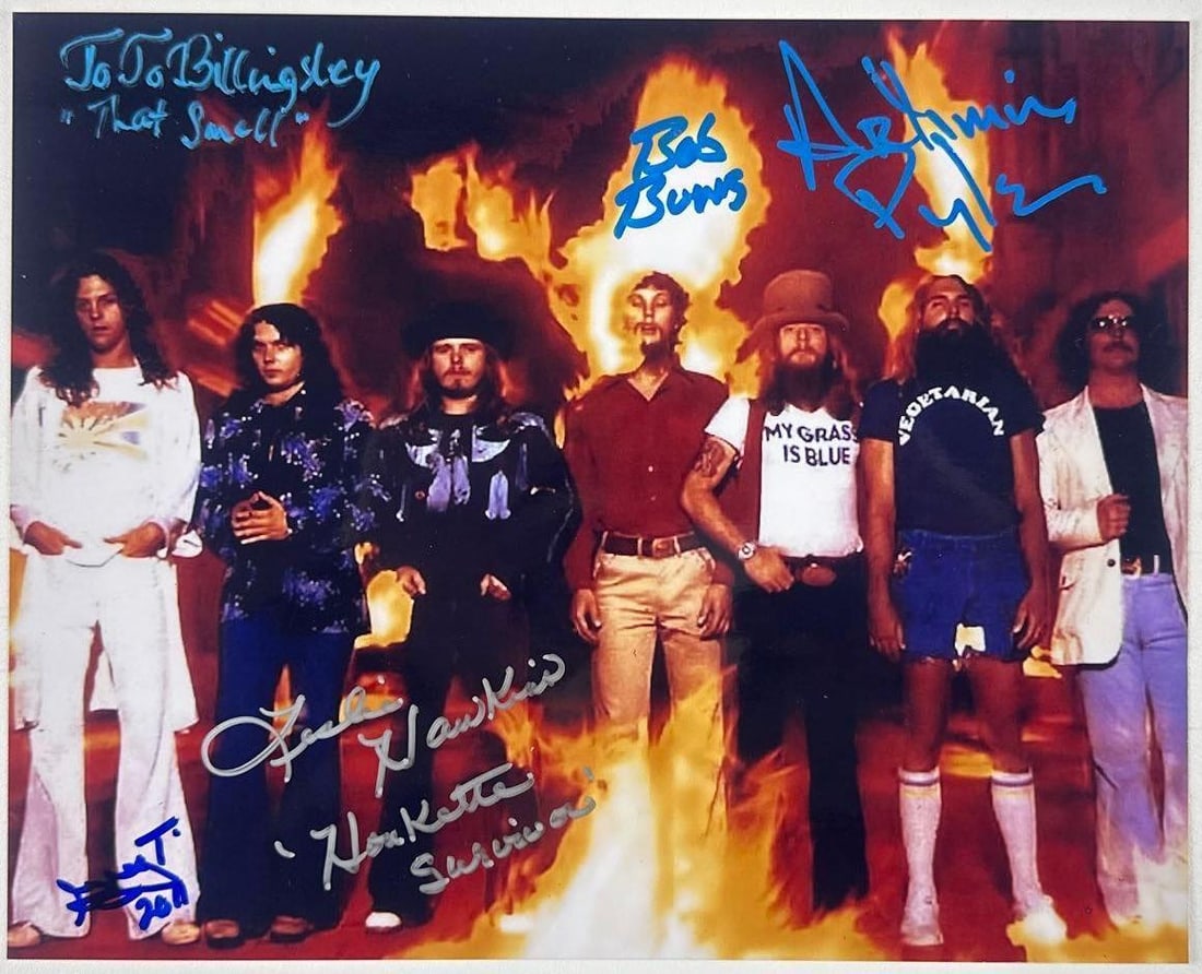 Lynyrd Skynyrd Group Signed 8.5" x 11" Photo (5 Sigs) (Beckett Authentication): Color 8.5" x 11" photo signed in blue paint pen and silver felt tip markers by Lynyrd Skynyrd band members Jo Jo Billingsley, who inscribed "That smell" after his signature, Bob Burns, Artimus Pyle, G
