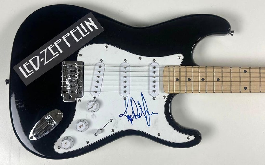 Led Zeppelin: John Paul Jones Signed Stratocaster-Style Electric Guitar (JSA): Black Stratocaster-style electric guitar signed on the pickguard in blue felt tip marker by Led Zeppelin band member John Paul Jones. Measuring approximately 39" x 13" and in fine condition.