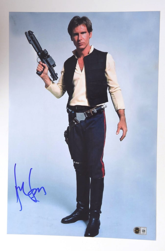 Star Wars: Harrison Ford Signed 18" x 12" Photo as Han Solo (Beckett Authentication): Color 18" x 12" photograph of Harrison Ford as the iconic character Han Solo from the "Star Wars" film franchise, signed prominently in blue felt tip marker by Ford. In fine condition. Authenticated b