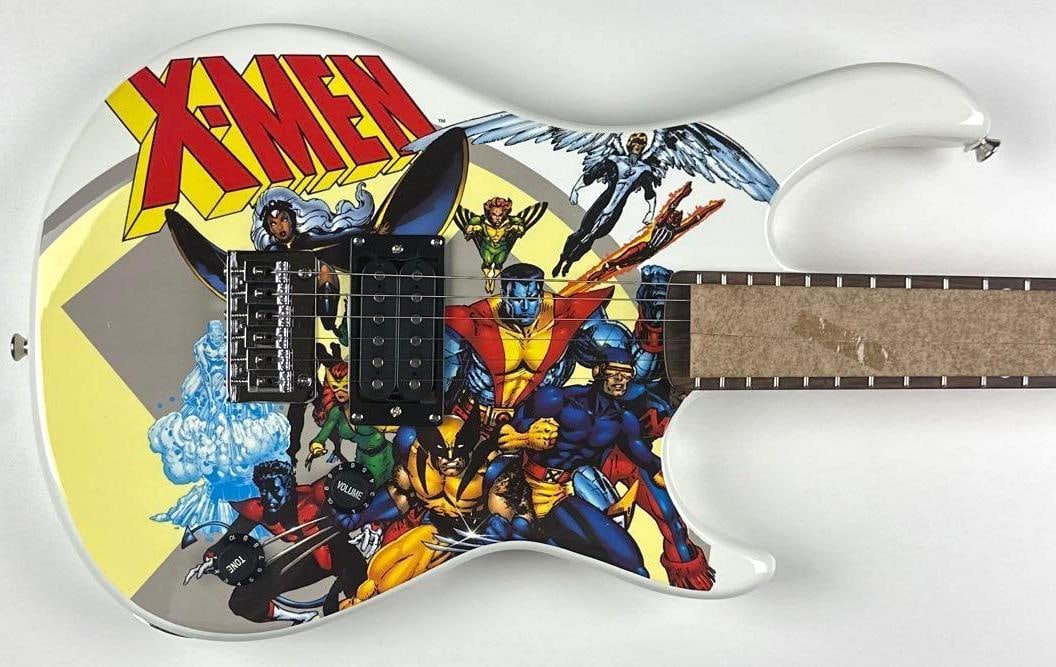 Marvel: X-Men Custom Graphics Stratocaster-Style Peavey Rockmaster Guitar: "Marvel" X-Men custom graphics Stratocaster-style Peavey Rockmaster guitar. Measuring approximately 38.25" x 11.75" x 2.25" and in fine condition. Unsigned guitar comes in original box.