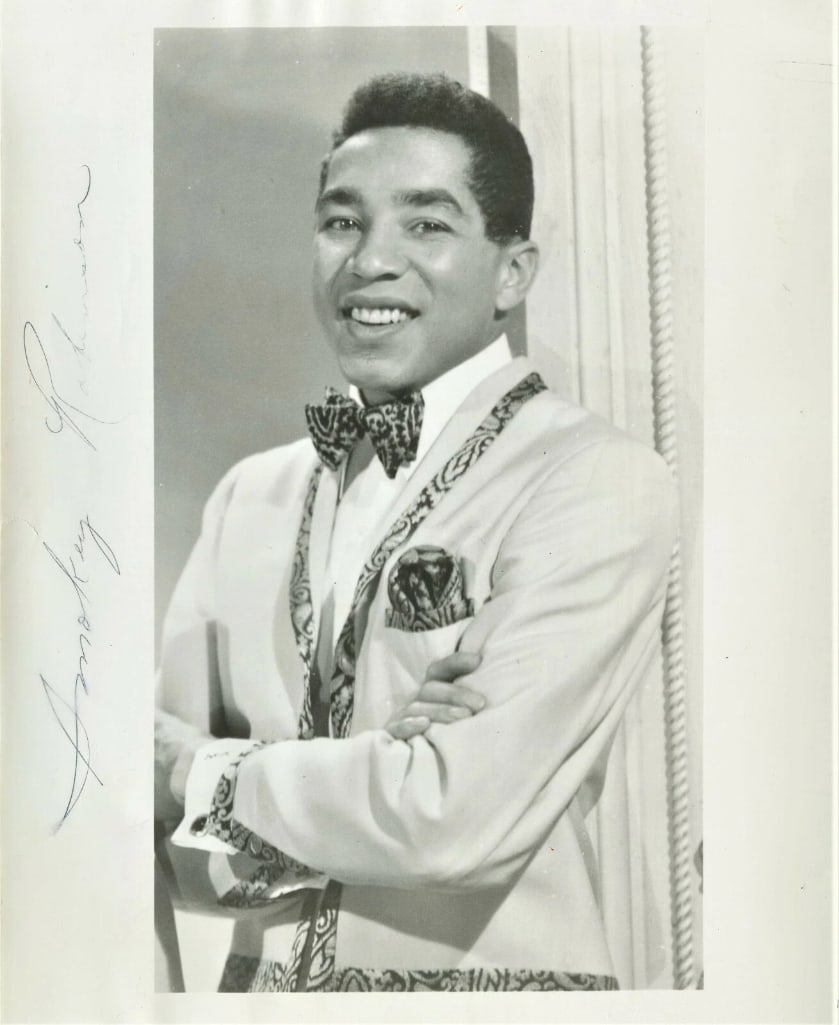 Smokey Robinson Signed 10" x 8" Photo (ACOA Authentication): Black-and-white 10" x 8" photo signed in black ballpoint pen by Motown singer Smokey Robinson. In very good condition, with some signs of scattered wear, including some small writing on the reverse,