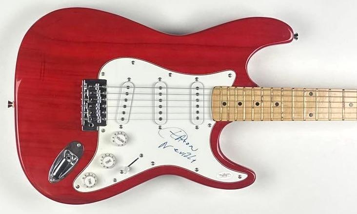 The Neville Brothers: Aaron Neville Signed Stratocaster-Style Guitar (JSA Authentication): Red Stratocaster-style Nomad brand guitar signed on the pickguard in black felt tip marker by musician Aaron Neville. Measuring approximately 39.5" x 12.75" and in fine condition. Guitar is accompanie