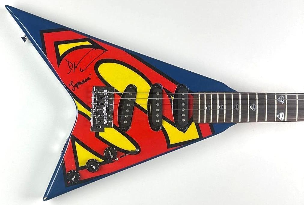 Superman: Dean Cain Signed & “Superman” Inscribed Custom Graphics V-Shaped Guitar: "Superman" custom graphics V-shaped guitar signed on the body in black felt tip marker by actor Dean Cain, who added his character name "Superman." Measuring approximately 44.5" x 16.75" and in fine c