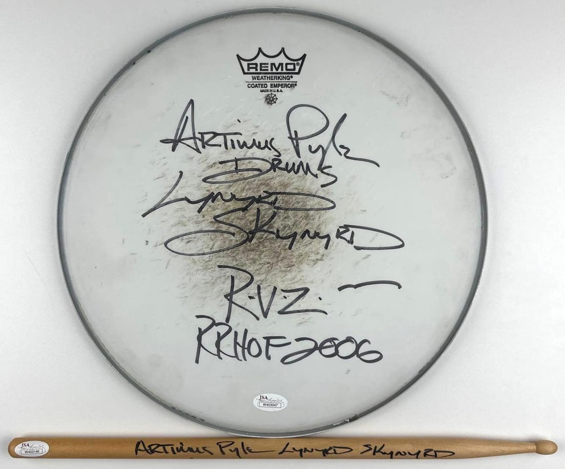 Lynyrd Skynyrd: Artimus Pyle Lot of (2) Signed 12.5" Drumhead & Drumstick (JSA Authentication): Group lot of two Artimus Pyle-signed items, consisting of a Remo drumhead and wooden drumstick. The white Remo drumhead, measuring approximately 12.5" x 12.5", is signed on the front in black