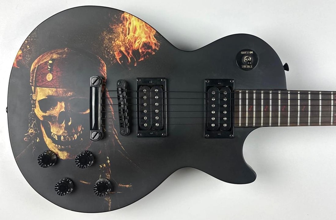 Pirates of the Caribbean Custom Graphics Les Paul-Style Epiphone Guitar: "Pirates of the Caribbean" custom graphics Les Paul-style Epiphone guitar. Measuring approximately 39.5" x 13" and in fine condition. The back of the fret on the spine has the inscription "A Pirate's