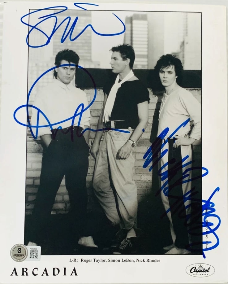 Arcadia Group Signed 10" x 8" Promo Photo (3 Sigs) (Beckett Authentication): Black-and-white 8" x 10" promotional photo signed in blue felt tip marker by Arcadia band members Roger Taylor, Nick Rhodes, Simon Le Bon. Obtained in-person. Accompanied by a full Letter of