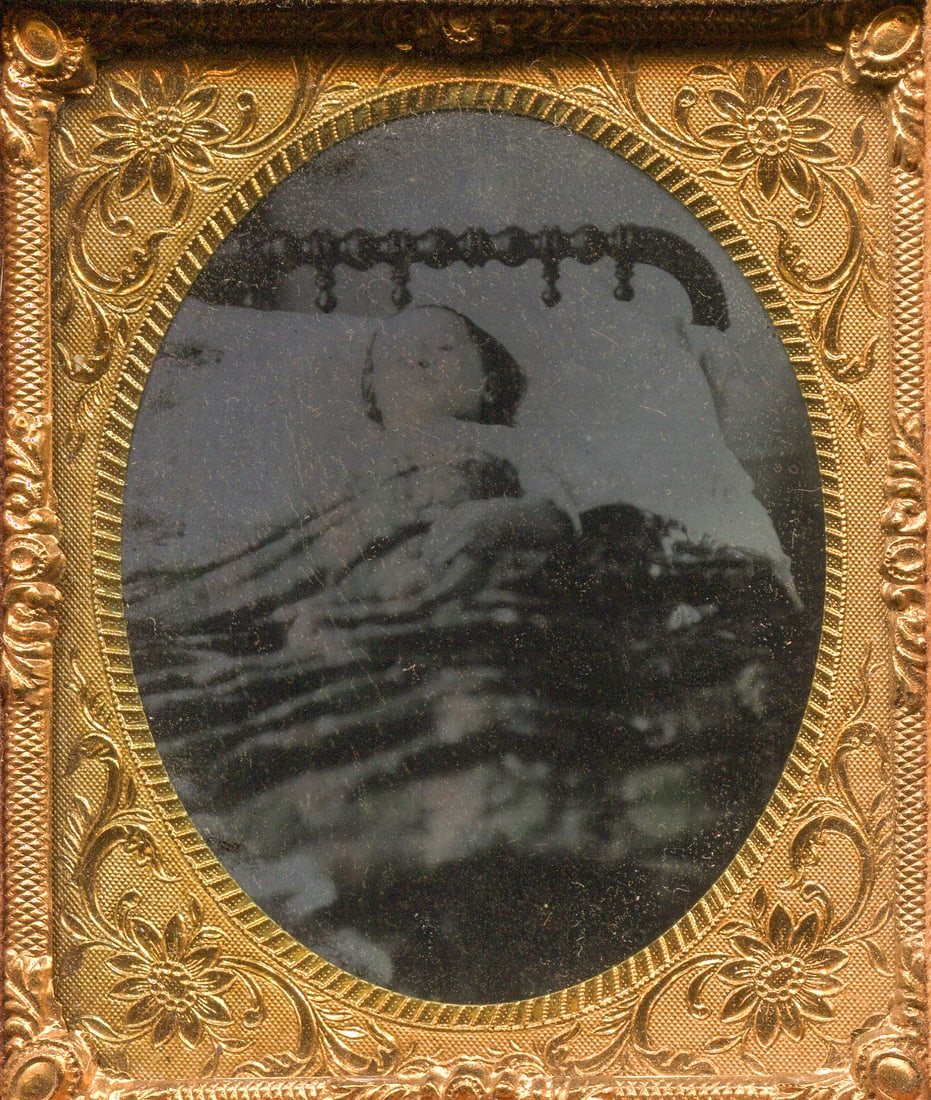 Post Mortem Ambrotype of a Child in Bed with Great Quilt: A poignant sixth plate ambrotype capturing a deceased child in repose on a bed, with particular attention drawn to the exquisite bed frame—the focal point of this solemn composition. Housed in a hal