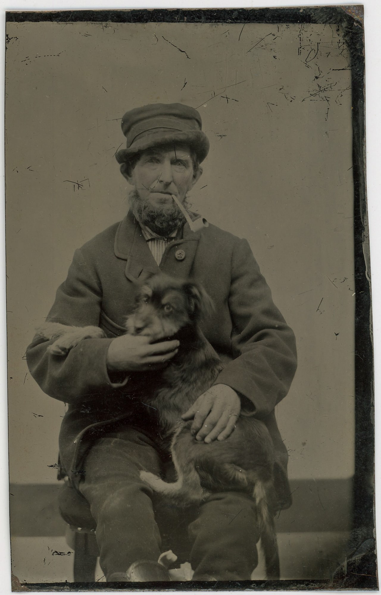 Tintype of a Man with his Clay Pipe and Terrier: A timeless CDV tintype capturing a man with his cherished clay pipe and faithful terrier by his side. In this evocative portrait, the man's rugged yet dignified demeanor reflects a life lived with sim