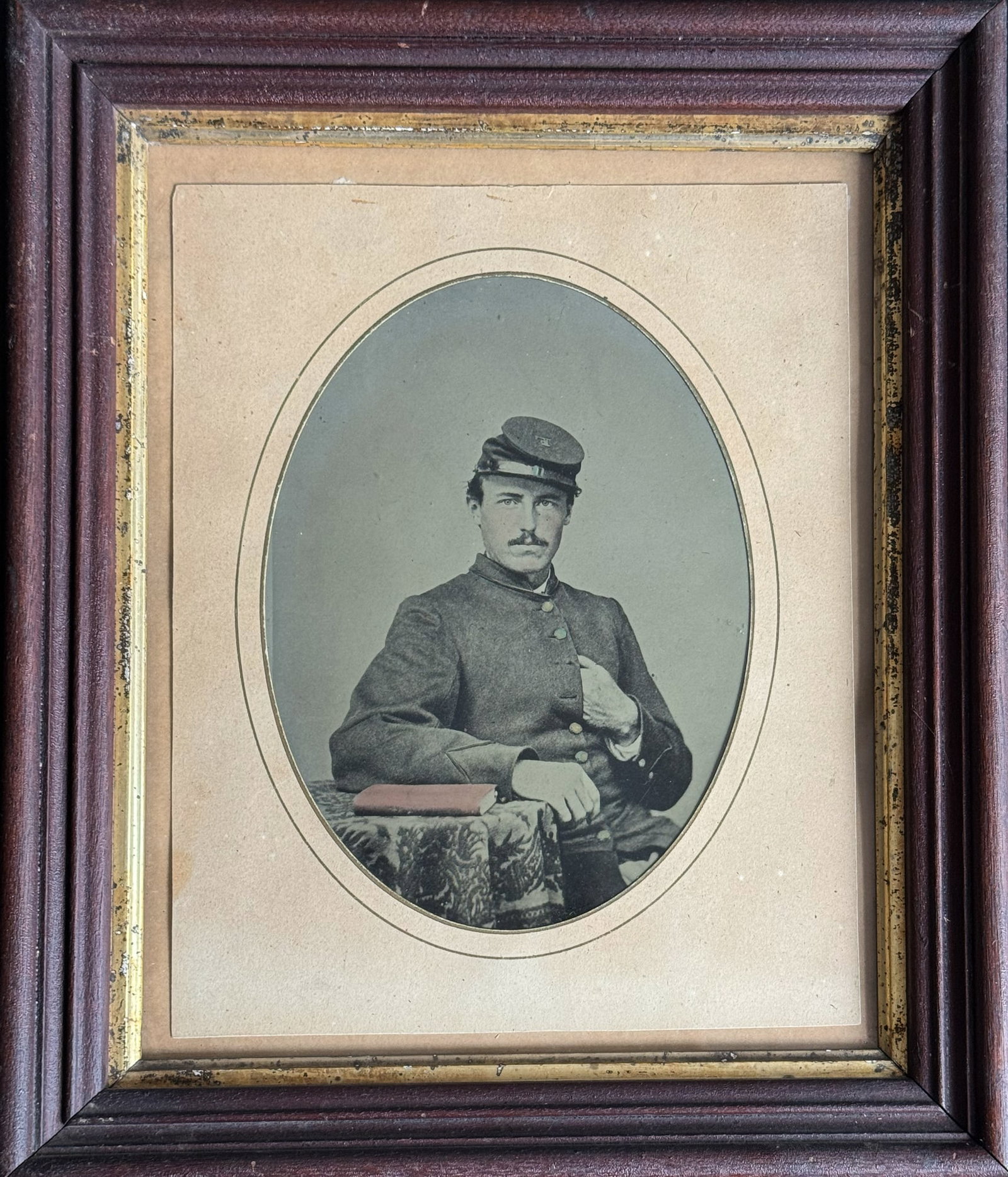 Framed Albumen Portrait of an Unidentified Union Soldier: Oval-format albumen portrait of a seated Union soldier, housed in its original wooden frame with gilt interior border. The young man is shown in standard issue military frock coat and forage cap, pose
