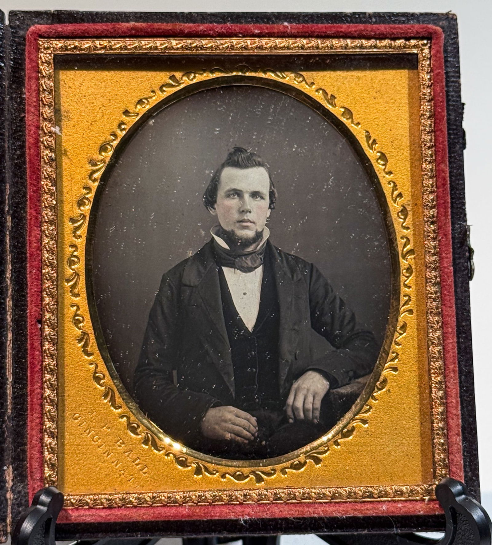 Daguerreotype Portrait by African American JP Ball: Sixth plate daguerreotype studio portrait of a young man seated and facing the camera, his right arm bent and resting at his side. He wears a dark jacket over a waistcoat with a high white shirt and c
