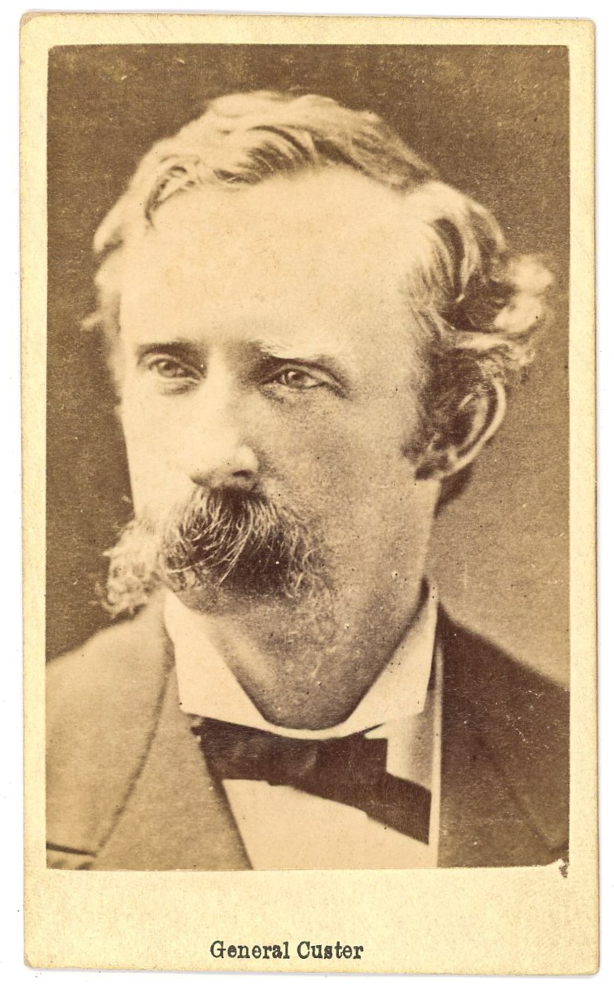 George Armstrong Custer, CDV Portrait, circa mid-1860s: Albumen carte de visite portrait of General George Armstrong Custer, depicted in civilian dress with his characteristic wavy hair and prominent mustache. The image is a tightly cropped head-and-should