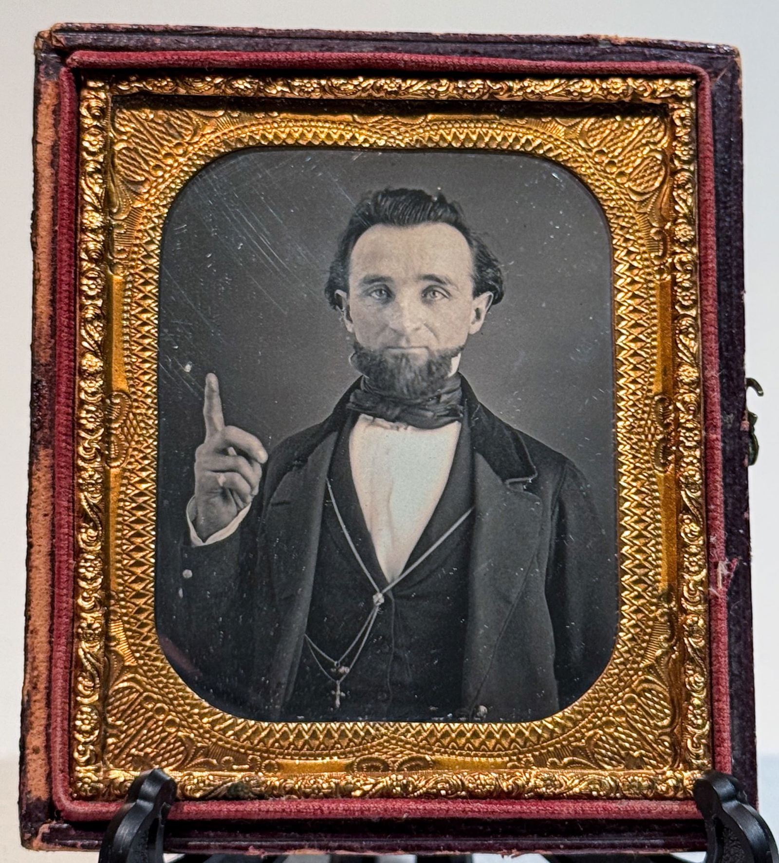 Daguerreotype Studio Portrait of Bearded Man Gesturing Upward: Sixth plate daguerreotype studio portrait of a bearded adult man posed half length, raising his right index finger upward in a deliberate gesture. He wears a dark coat over a waistcoat and light shirt