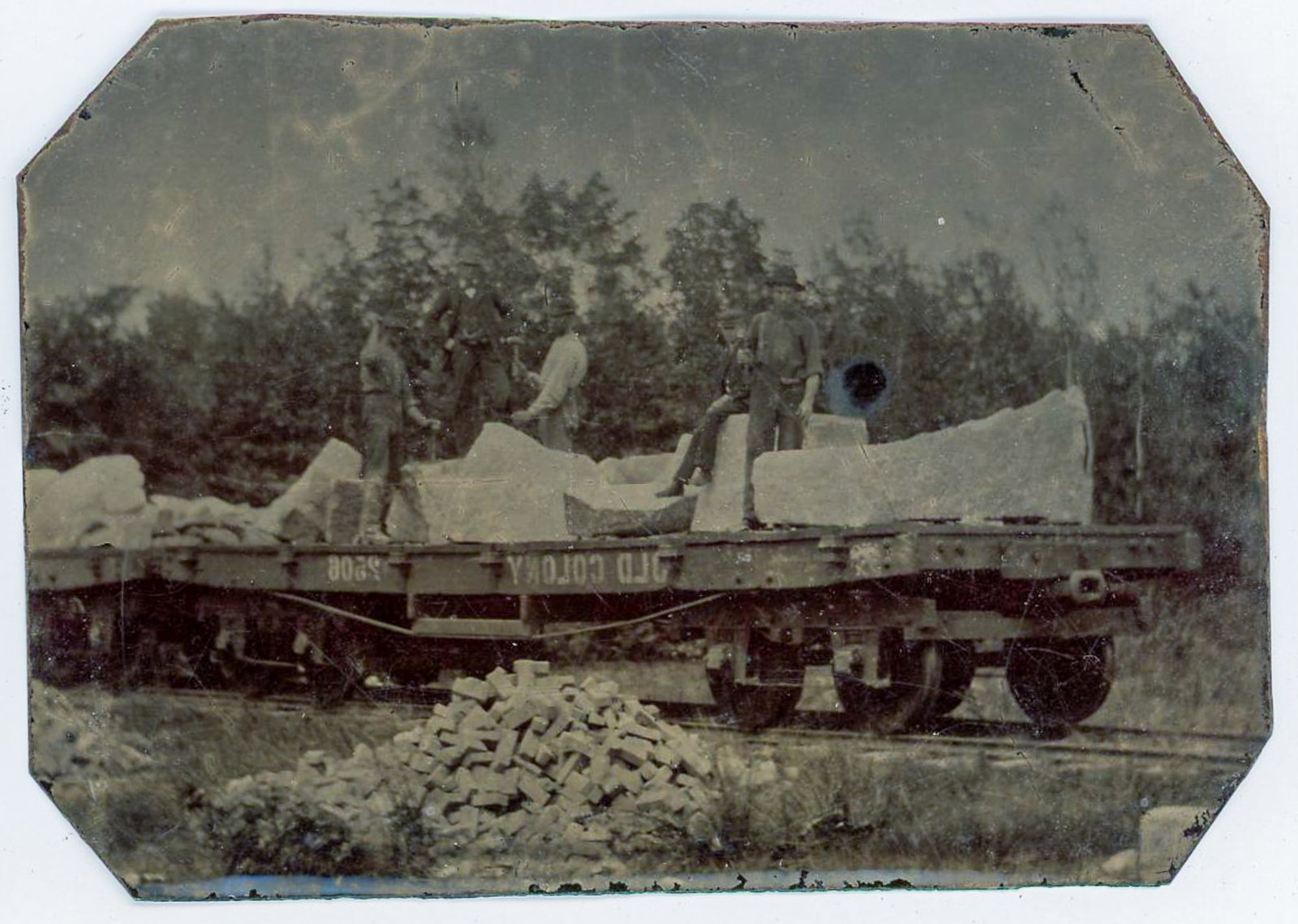 Tintype of Railroad Laborers on Flatcar Loaded with Stone Blocks: Tintype photograph depicting a group of laborers standing and working atop a railroad flatcar loaded with large cut stone blocks, likely intended for construction or track-related infrastructure. The