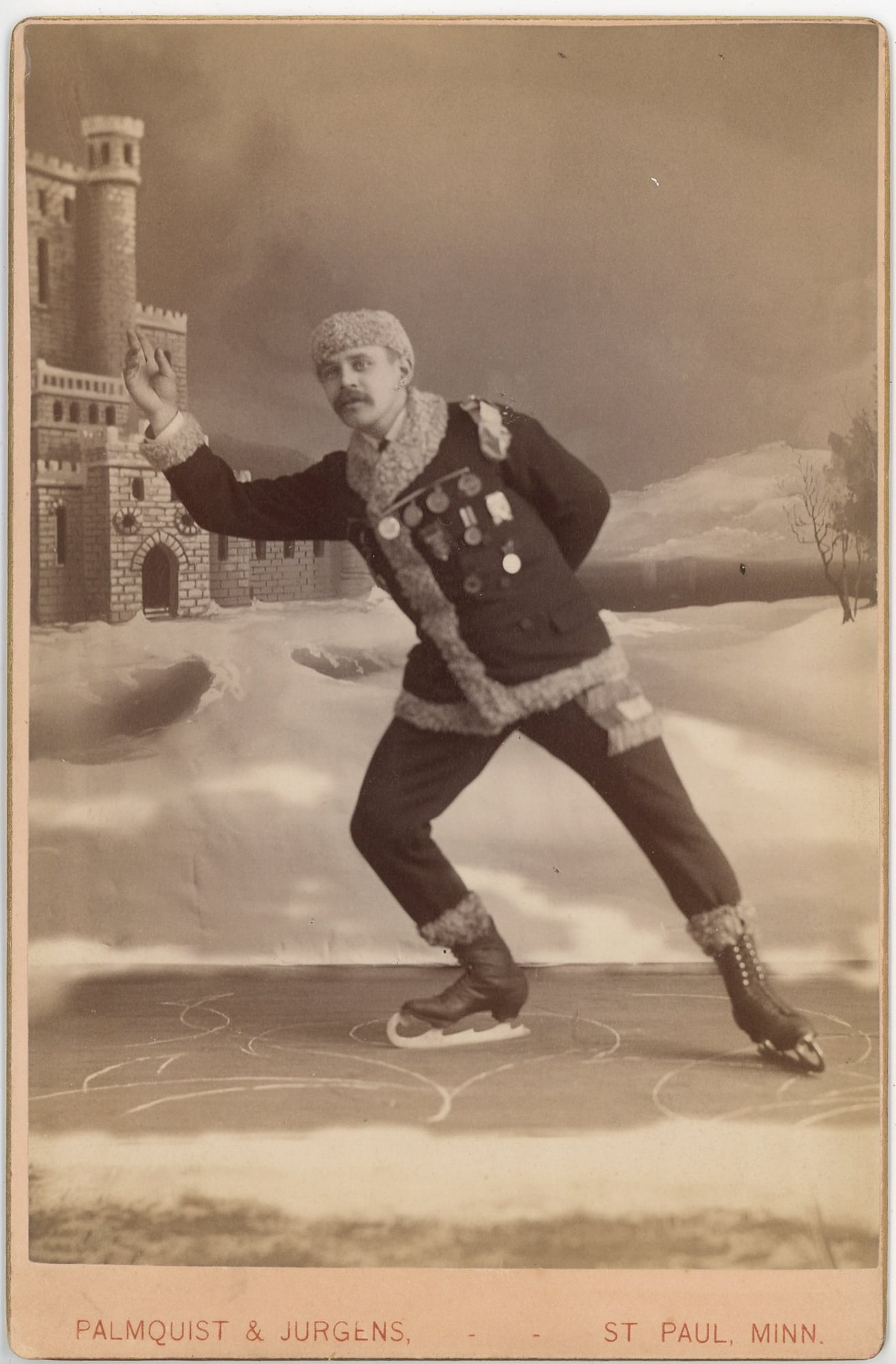 Cabinet Card of Ice Skater in Fur-Trimmed Costume, St. Paul: Cabinet card studio photograph depicting a male ice skater captured in a dynamic skating pose, wearing a heavy fur-trimmed costume and skates, with multiple medals pinned across his chest. The scene i