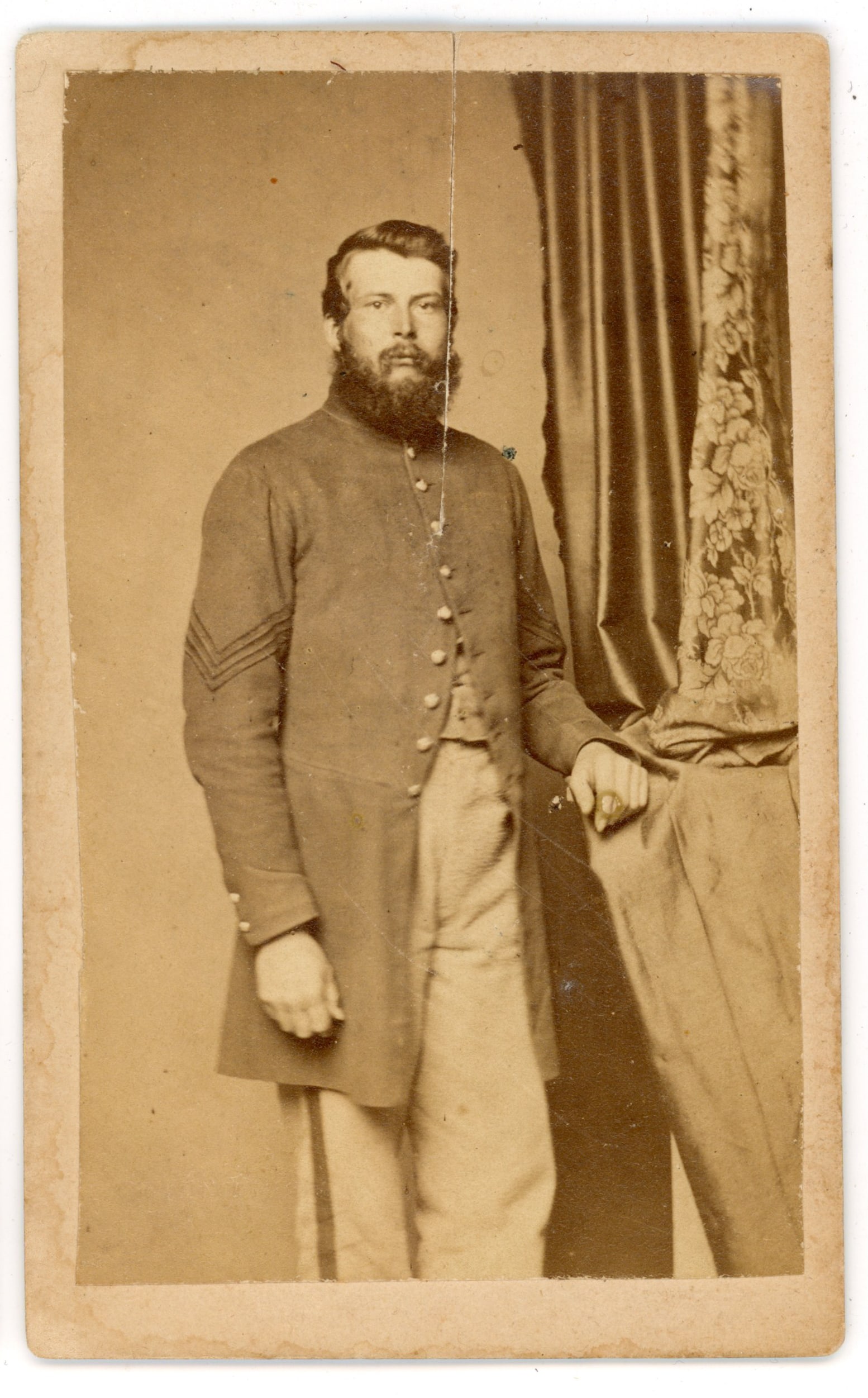 CDV Union Sergeant Wolff Gallery Alexandria VA: Carte de visite portrait of an unidentified Union Army sergeant standing beside a draped studio table. The soldier wears a military frock coat with sergeant’s chevrons clearly visible on the sleeve,