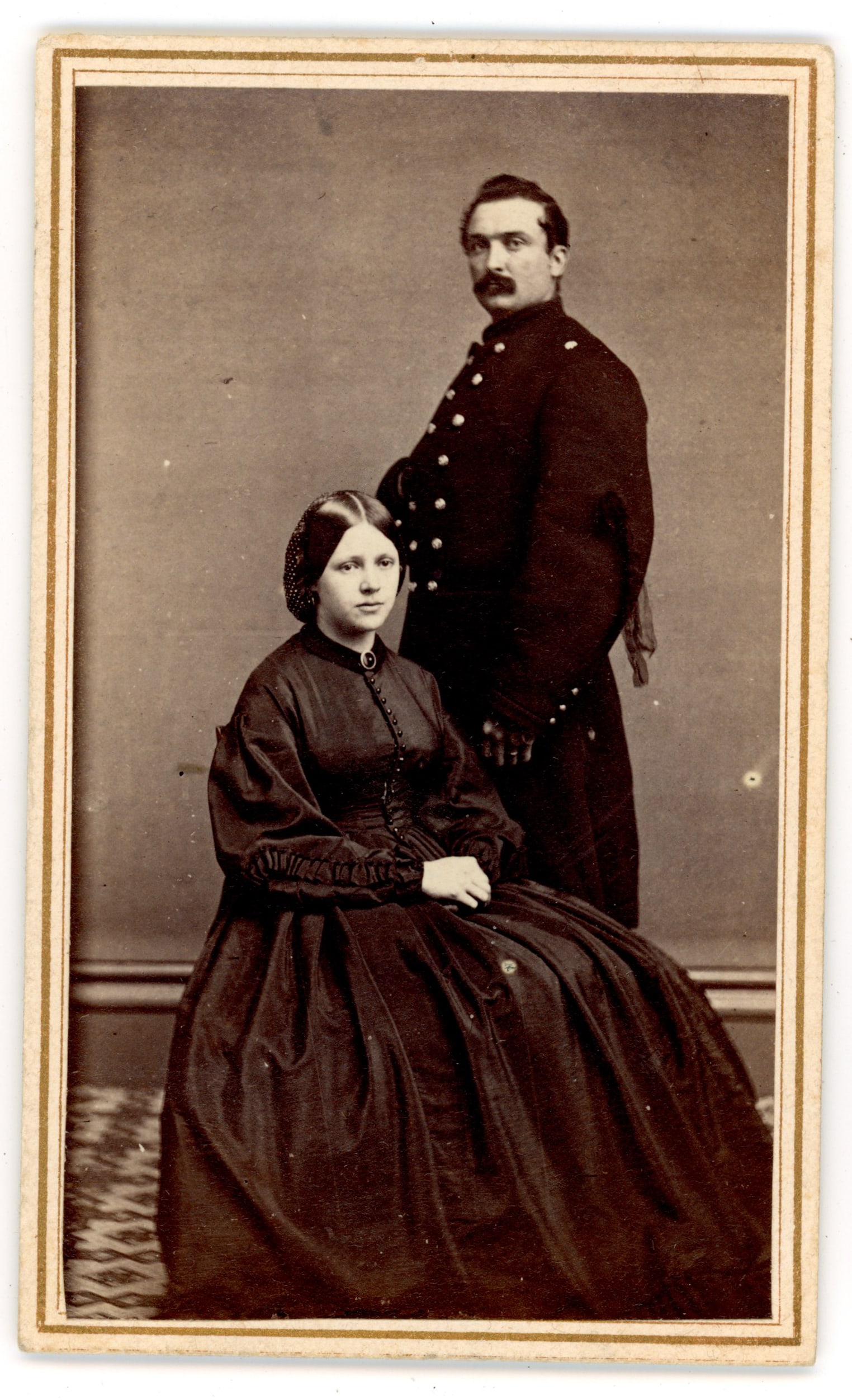 CDV Union Soldier with Wife Portrait: Carte de visite photograph depicting an unidentified Union soldier standing beside a seated woman, likely his wife or family member. The soldier wears a military frock coat while the woman sits in a f
