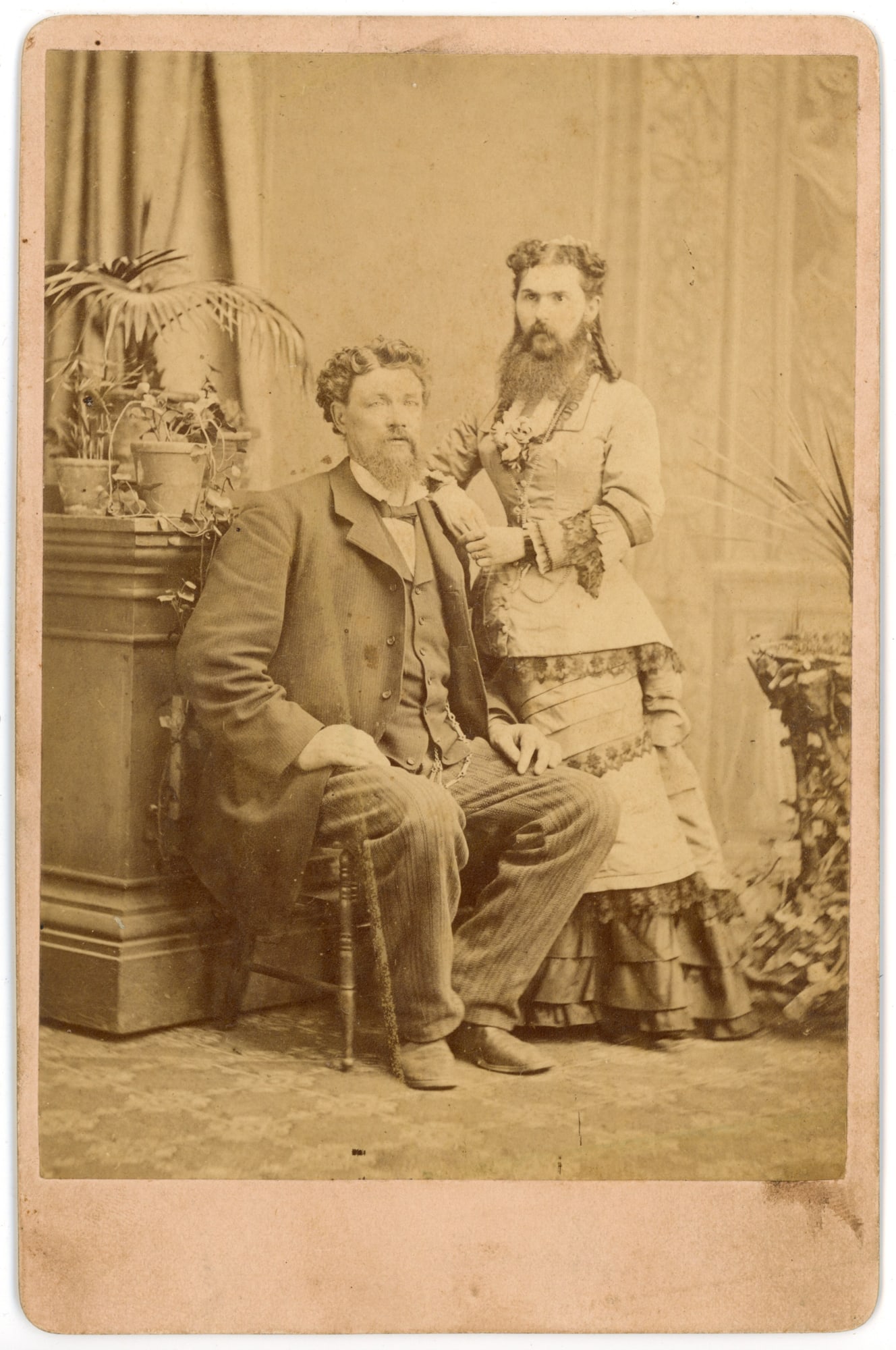 Bearded Woman Mrs. Meyers Cabinet Card Portrait, 19th Century: Albumen cabinet card portrait depicting Mr. & Mrs. A. Myers, with the bearded woman standing beside her seated husband in a studio interior. The woman wears a fitted dress with decorative trim and hol
