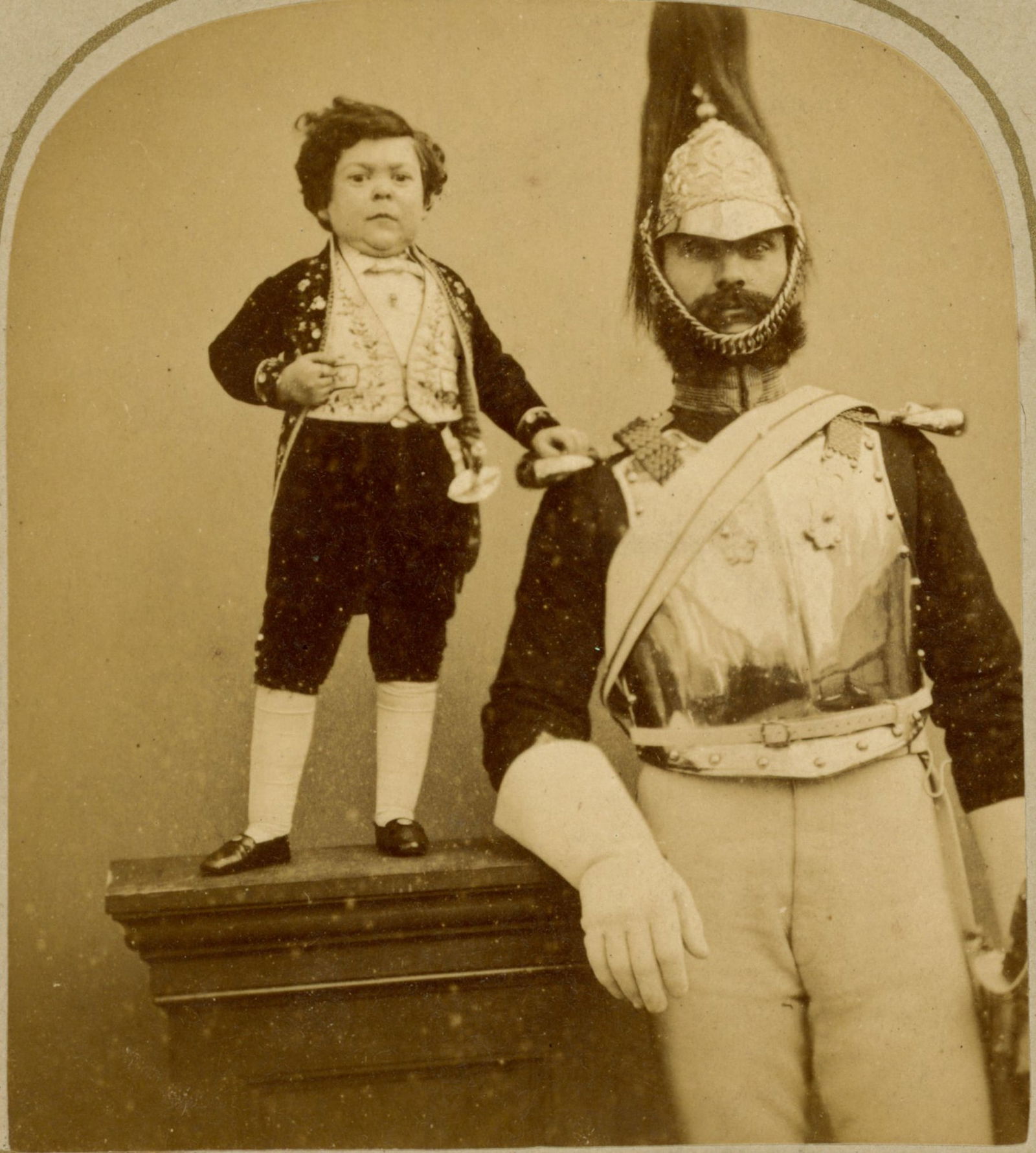 General Tom Thumb AKA Charles S. Stratton Stereoview, 1864: Albumen stereoview depicting General Tom Thumb (Charles S. Stratton) standing beside a uniformed military figure. Stratton is shown posed on a pedestal, wearing formal attire with vest and bow tie. Th