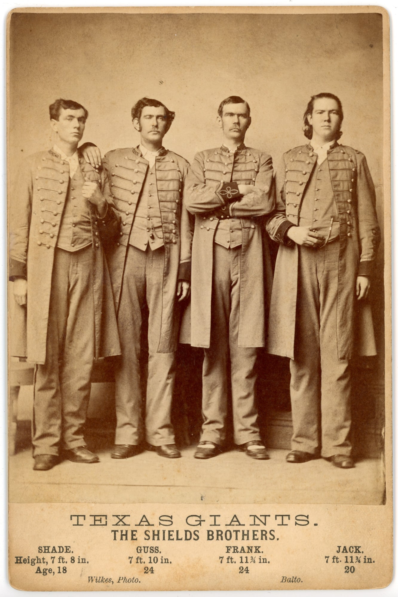 Cabinet Card Texas Giants Shields Brothers Wilkes: Cabinet card photograph titled “Texas Giants. The Shields Brothers.” showing four exceptionally tall men standing side by side in uniform-style coats with decorative frogging and long overcoat