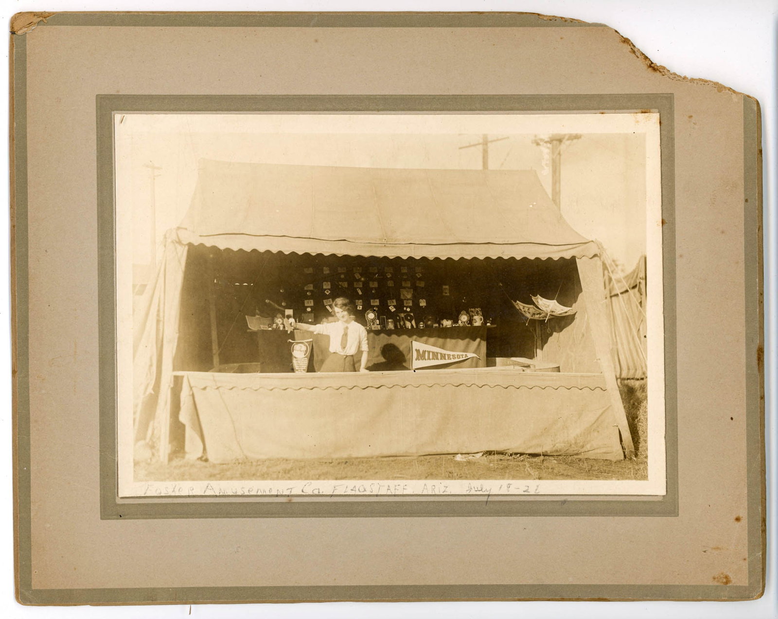 Photograph, Carnival Game Booth, Flagstaff Arizona: Gelatin silver photograph depicting a carnival or fairground game booth, mounted on a larger card, early 20th century. The image measures approximately 5 x 7 inches on an 8 x 10 inch mount. A handwrit